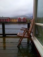 wooden chair on terrace in view of colorful buildings on coast, norway