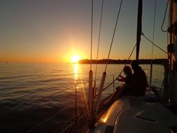 silhouettes of people on a sailing boat at sunset