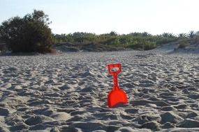 red children's shovel in the sand on the beach