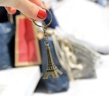 small eiffel tower in womanâs hand, colorful bags at background, shopping concept