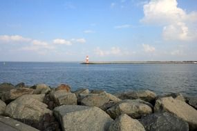 view of distant lighthouse on mole from rocky sea coast