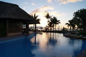 luxury swimming pool in front of tropical beach at sunset