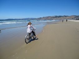 young girl riding bicycle on coast at water, usa, california, pismo beach