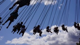 people selhouettes on chain swing at sky
