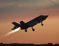 Take-off of a military fighter aircraft at beautiful colorful sunset