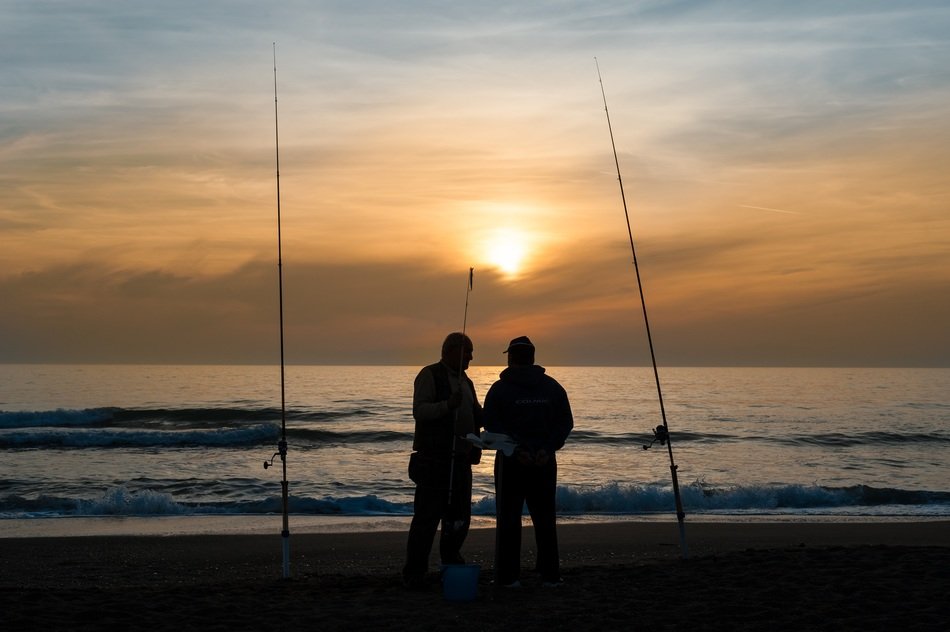 fishermen with fishing rods on the beach at sunrise