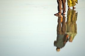 feet reflected in the water on the beach