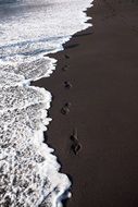 footprints on the black sand near the water