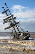 leaning sailing ship on stormy sea at coast