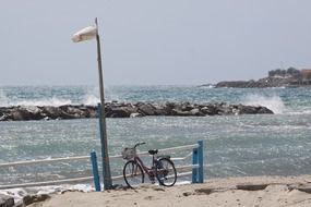 a bicycle stands near a pillar on the shore