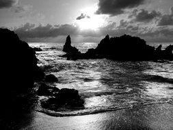 black and white photo of rocks on ocean and beach