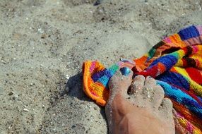 A view of the foot on the beach, which stands on a colorful towel