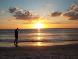 man walks along the ocean beach at sunset