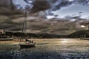 sailboat on dark glossy water in view of beach