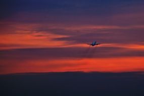 plane flies in the red sky during sunset