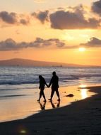 romantic couple walks along the beach at dusk in California