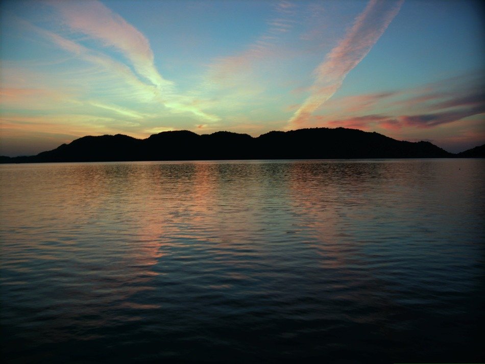 the sun behind the mountains near the sea