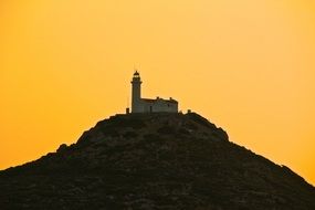 lighthouse on a high hill against a yellow sky
