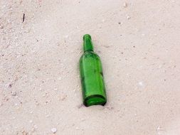 empty green bottle on sandy beach