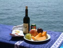 bottle of wine and fruit served next to the sea