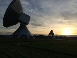 two large satellite dishes in sunset landscape