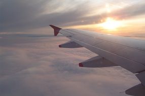 airplane wing above the clouds during sunset