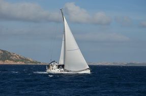 white sailboat on the blue water on the background of the coast