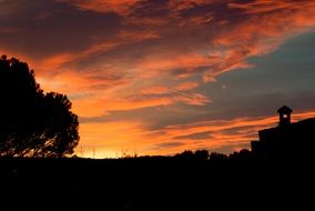 red sunset clouds and dark trees silhouettes at twilight
