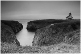 black and white photo of the lighthouse at ocean shoreline