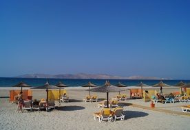 Colorful sun loungers with parasols on the sandy coast