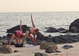 man and woman practicing yoga on beach at sea