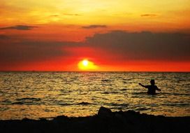 man bathes in the sea at sunset