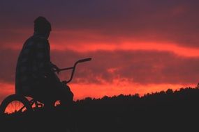 dark male silhouette on bicycle at red sunset sky