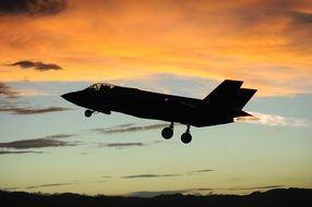 silhouette of taking off military jet at sunset sky