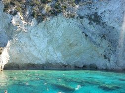 people swimming in turquoise sea at white cliff, greece, zakynthos