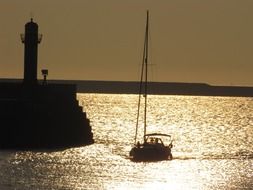 lighthouse and sailboat in the shining water