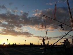 children on rope attraction silhouettes at sunset sky, germany, sylt