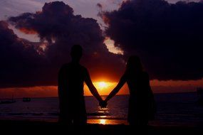 silhouette of couple holding hands at sunset beach