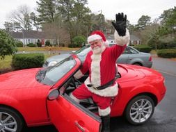 Santa Claus sits in a sports red car