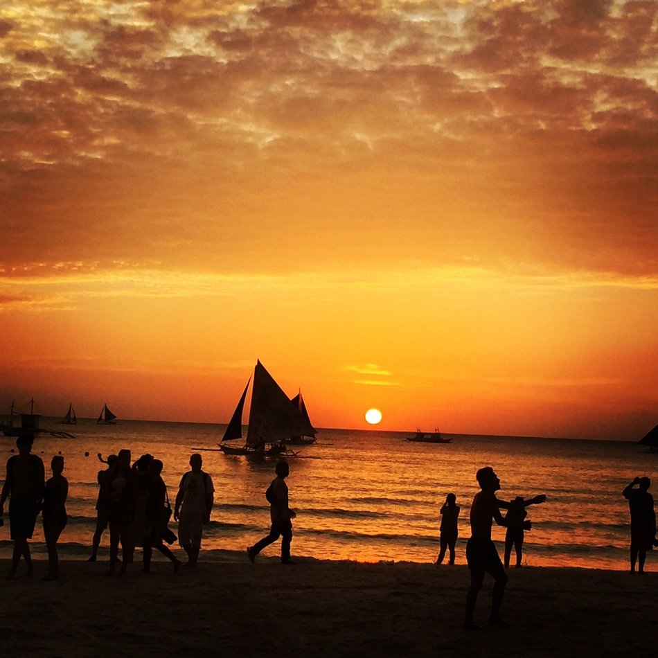 very beautiful philippines sunset with the silhouettes of people and boats on the water