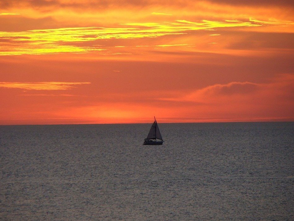 landscape of sail boat in sea under orange sunset sky