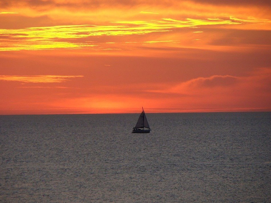 landscape of sail boat in sea under orange sunset sky