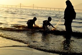 children with mom splash on the evening beach