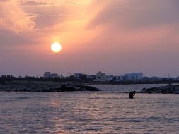 person stands alone in water near coast at sunset