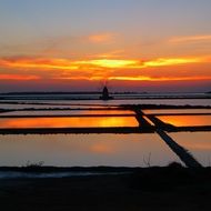 windmill at water in sunset landscape, italy, marsala, saline