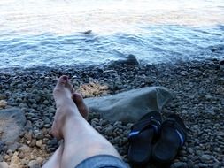 man lies on pebbles on the coast