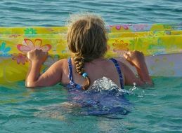 girl swims in the sea with a mattress