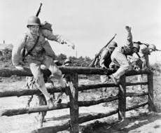 black and white photo of a soldier jumping over an obstacle