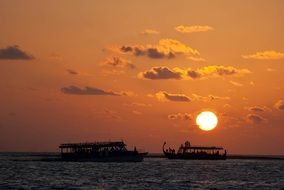silhouettes of two boats with people on sea at sunset