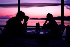 silhouettes of people at a table in a cafe at sunset
